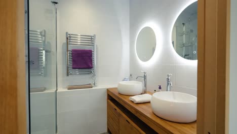Modern-designed-bathroom-for-2-persons,-led-lights-behind-the-mirrors-with-wooden-basin