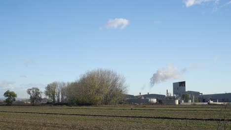 Toma-Estática-De-Una-Industria-Agrícola-Rural-Que-Emite-Humos-Contaminantes-En-Una-Zona-De-Agricultura-Orgánica.
