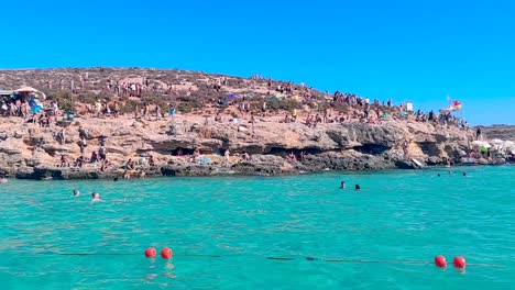 Panning-shot-from-a-touristic-boat-towards-the-rocky-beach-in-Blue-Lagoon-Bay-at-Comino-Island-in-Malta
