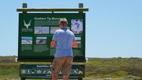 Southern-Tip-Monument-information-board-with-tourists-visiting-site,-Agulhas