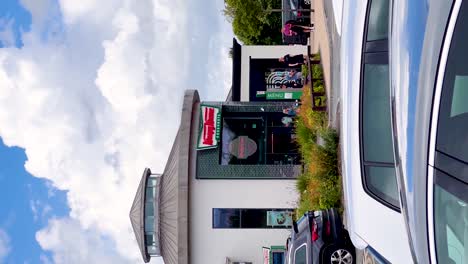 Sunny-Delights:-Vertical-Video-of-Krispy-Kreme-in-Blanchardstown-Town,-Bustling-with-Cars,-Donut-Enthusiasts,-and-Urban-Vibes