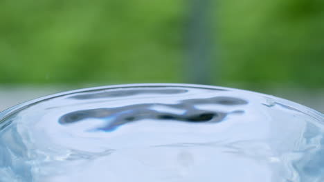 Wassertropfen-Erzeugen-Wellen-Und-Oberflächenspannung,-Was-Zu-Einer-Bewegung-Des-Wassers-In-Einem-Klarglasbehälter-Führt