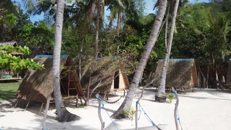 Eco-stilt-hut-bungalows-and-palm-tree-hammock-swing-on-tropical-white-sand-beach