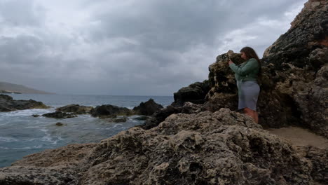 Mittelgroße-Handaufnahme-Vor-Der-Küste-Maltas-Mit-Blick-Auf-Eine-Reisende-Influencerin,-Die-Die-Felsen-Und-Wellen-Des-Meeres-Für-Ihren-Social-Media-Beitrag-Auf-Ihrer-Aufregenden-Urlaubsreise-Fotografiert