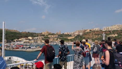 Handheld-shot-of-tourists-during-a-ferry-ride-into-the-port-of-malta-with-a-view-of-the-historic-buildings,-the-blue-sea-and-photographing-travelers-on-a-hot-summer-day