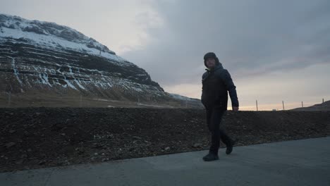 Man-walk-on-concrete-pavement-near-huge-Icelandic-mountain-during-sunset