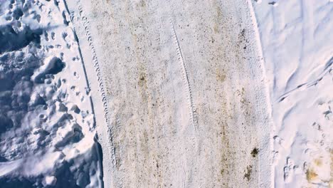 Snow-Covered-Winding-Road-Neighborhood-or-Long-Driveway-with-Tire-Tracks-and-Mud-Streaks-Packed-in-with-Footprints