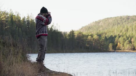 Man-Standing-By-The-Lake-Looking-Through-The-Binoculars