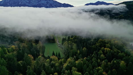 Misty-forest-with-mountain-backdrop-covered-with-clouds,-drone-pan-shot,-Attersee,-Austria