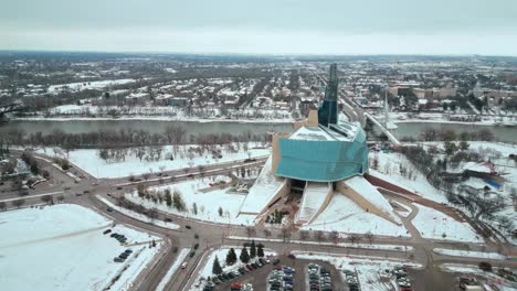 Toma-De-Establecimiento-Museo-Canadiense-De-Derechos-Humanos-Urbano-Winnipeg-Manitoba-Canadá-Centro-Rascacielos-Edificios-En-La-Ciudad-Paisaje-Nublado-Horizonte-Nevando-Invierno-Drone-4k-Disparo-Amplio-Cinematográfico