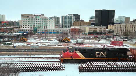 4K-Static-Time-Lapse-Drone-Shot-Colorful-Steel-Transport-Industrial-CN-Rail-Industrial-Train-Steam-Coal-Locomotive-Driving-Through-Downtown-Winter-Urban-Winnipeg-Manitoba-Canada