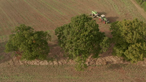 Pan-down-aerial-shot-over-a-tractor-ploughing-around-large-trees