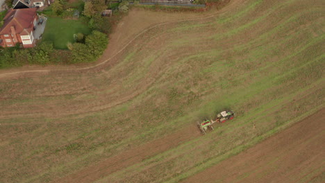 Pan-down-aerial-shot-over-a-tractor-ploughing-a-field-near-a-village
