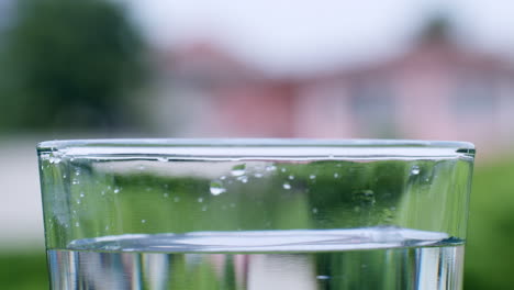 Winzige-Tröpfchen-Spritzen-In-Ein-Mit-Mineralwasser-Gefülltes-Glas-Und-Erzeugen-Am-Rand-Wellen-Und-Wellen