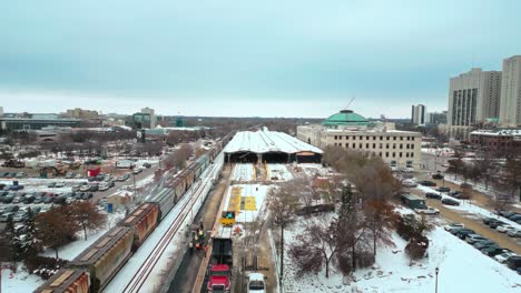4K-Wide-Drone-Tracking-Shot-Industrial-Steam-Train-Pulling-in-to-CN-Rail-Railway-Transport-Station-in-Daytime-Snow-Covered-Winter-Downtown-Urban-Winnipeg-Manitoba-Canada