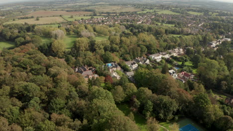 Rising-aerial-shot-over-dense-forest-towards-small-english-town-Theydon-Bois