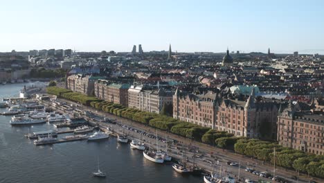 Verkehr,-Fußgänger-Und-Boote-Im-Dock-Auf-Strandvägen-Und-Strandkajen,-Stockholm-An-Einem-Sonnigen-Abend-Mit-Alten-Wohnhäusern-Und-Sichtbarer-Skyline