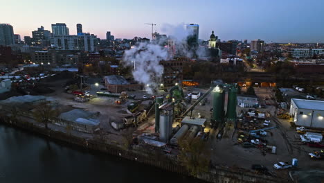 Aerial-view-circling-a-smoking-chimney-at-the-Ozinga-Concrete,-dusk-in-Goose-Island,-Chicago