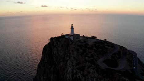 Historic-old-lighthouse-on-the-edge-of-cliff-at-sunset-orange-light-shadows,-drone-aerial