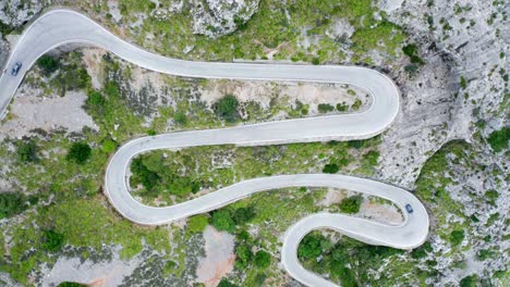 Cars-on-winding-curvy-road-through-green-forested-stony-mountain-range,-drone-aerial-view