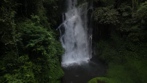 A-powerful-waterfall-in-the-depths-of-Balinese-jungle-on-an-overcast-afternoon,-aerial