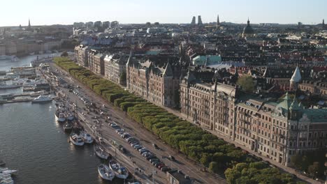 Traffic-and-pedestrians-on-Strandvägen-and-Strandkajen,-Stockholm-during-sunny-evening-with-old-apartment-buildings-and-skyline-visible