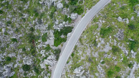 Curvy-lone-road-through-green-stony-mountain-range-remote-pass,-drone-aerial-view