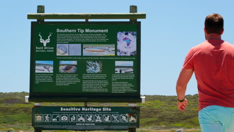 Man-walks-up-to-read-information-board-of-Southern-Tip-Monument,-Cape-L'Agulhas