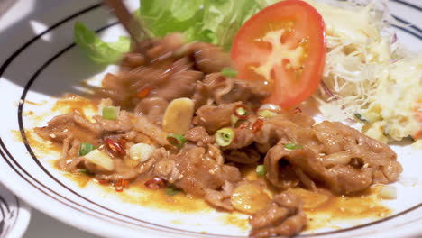 Mixing-a-plateful-of-spicy-stir-fried-meat-with-vegetable-salad-of-sliced-tomato,-lettuce,-and-cabbage-on-the-sides
