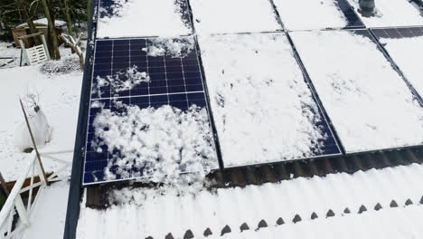 Aerial-view-around-wet,-partly-snowy-solar-cells-on-a-house-roof,-winter-day