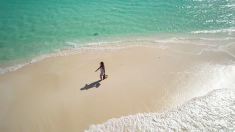 Aerial-view-woman-in-white-dress-and-straw-hat-in-hands-on-beautiful-deserted-beach