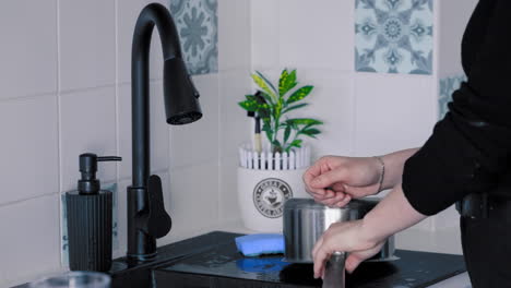 Medium-shot-of-a-young-Woman-wearing-black-clothes-washing-dishes-with-soap-in-black-kitchen-Sink-under-running-water-in-slow-motion