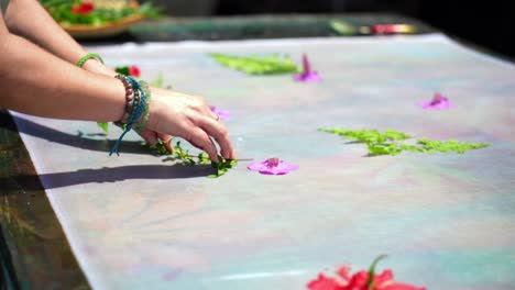 Clients-learning-homemade-batik,-sarong,-pareo,-placing-green-leaves-and-flowers-on-white-cloth,-Mahe-Seychelles-25fps-1