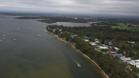 Aerial-drone-shot-tracking-a-boat-moving-down-the-Shoalhaven-river-on-a-stormy-day-in-South-coast-NSW,-Australia