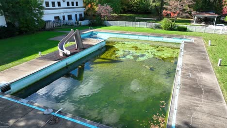 Neglected-swimming-pool-with-algae-growth-and-a-slide
