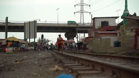Slum-area-in-Accra,-Ghana-with-train-tracks-and-people-walking-by-wearing-traditional-Ghanaian-cloth