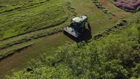 Aerial-footage-of-a-farmer-cutting-grass-with-his-green-combine-on-a-sunny-day
