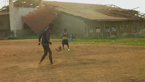 Young-man-showing-off-his-fancy-football-juggling-skills-to-his-friends-on-a-dry-dusty-community-football-field,-Kumasi,-Ghana