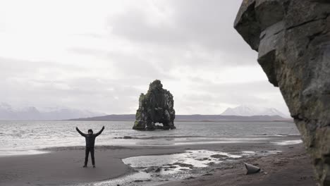 Reveal-shot-of-man-standing-on-black-sand-beach-near-Hvitserkur-rock
