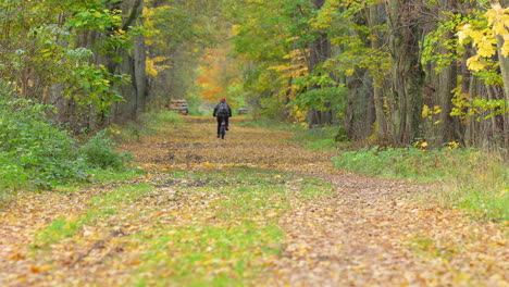 Cyclist-rides-down-leaf-covered-forest-trail-in-fall