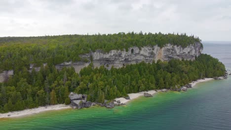 Rocky-coastline-overgrown-with-forest-near-lake,-aerial-view