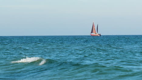 Ein-Einzelnes-Segelboot-Mit-Roten-Segeln,-Das-Auf-Einem-Ruhigen-Blauen-Meer-Unter-Klarem-Himmel-Schwimmt