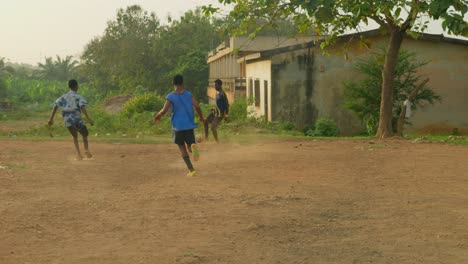 Un-Joven-Pasa-El-Balón-A-Un-Compañero-De-Equipo-Y-Luego-Lo-Devuelve-Mientras-Se-Los-Ve-Jugando-Al-Fútbol-En-Un-Polvoriento-Campo-De-Fútbol-Comunitario-En-Kumasi,-Ghana.