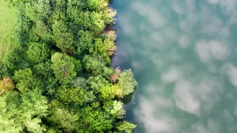 Clouds-are-reflected-in-a-river-next-to-a-lush-green-forest,-aerial-top-view-birdseye-drone