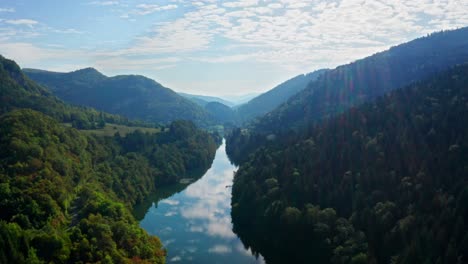 Sonnenstrahlen-Fallen-Auf-Einen-Reflektierenden-Fluss,-Der-Durch-Eine-Bewaldete-Hügellandschaft-Fließt,-Drohne-Aus-Der-Luft
