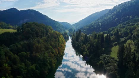 Blau-Reflektierender-Fluss-Zwischen-Bewachsenen-Bergen-In-Einer-Idyllischen,-In-Sonnenlicht-Getauchten-Landschaft