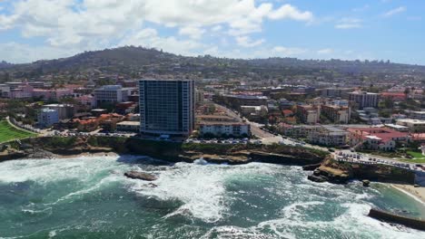 Aerial-View-Of-High-rise-Office-Building-With-Waves-Crashing-On-Shell-Beach-And-Children's-Pool-La-Jolla-In-California,-United-States