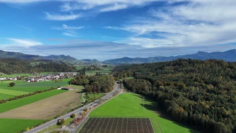 Aerial-Flying-Over-Countryside-Rapperswil-Jona-And-Forest-Trees-With-Highway-Road-Running-Through-It