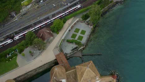 Switzerland-city-aerial-view-A-bullet-train-is-moving-on-a-riverside-road,-with-four-wheels-and-a-bus-beside-it