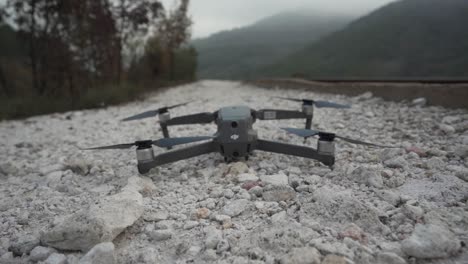 A-DJI-drone-is-seen-taking-off-from-white-gravel-next-to-a-railroad-revealing-mountains-and-forest-then-the-tracks-vanishing-into-the-landscape